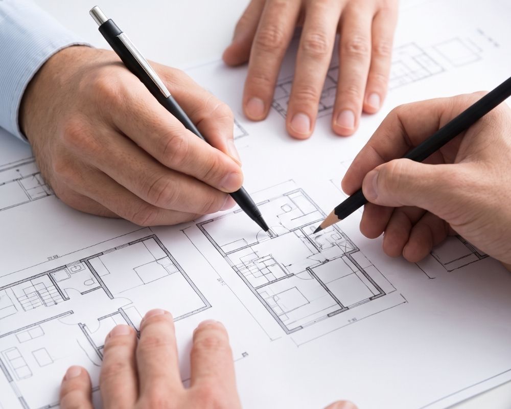 Close-up of an architect's hands expertly sketching custom modifications onto a set of printed residential floor plans.